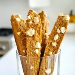 To make pumpkin spice biscotti, you'll need some key ingredients. Here’s a simple list: - 1 cup pumpkin puree - 2/3 cup granulated sugar - 1/2 cup brown sugar - 1/4 cup vegetable oil - 3 large eggs - 2 teaspoons vanilla extract - 3 1/2 cups all-purpose flour - 2 teaspoons baking powder - 1 teaspoon baking soda - 1 tablespoon pumpkin spice blend (or a mix of cinnamon, nutmeg, ginger, and allspice) - 1/2 teaspoon salt - 1/2 cup chopped walnuts or pecans (optional) - 1/2 cup white chocolate chips (optional) Each ingredient plays a vital role in your biscotti. Pumpkin puree adds moisture and flavor. The sugars give sweetness and a nice golden color. Vegetable oil keeps the biscotti tender. Eggs provide structure and richness. When you combine the flour with baking powder and baking soda, you create a light texture. Pumpkin spice blend brings warmth with its fragrant mix of spices. Salt enhances all the flavors. The optional mix-ins, like nuts and white chocolate, add texture and extra flavor. Feel free to get creative with these additions! - Preheat your oven to 350°F (175°C) and line a baking sheet with parchment paper. - In a big bowl, whisk together the pumpkin puree, granulated sugar, brown sugar, and vegetable oil. Mix until smooth. - In another bowl, combine all-purpose flour, baking powder, baking soda, pumpkin spice blend, and salt. Gradually add this dry mix to the wet ingredients. Stir until just combined. - Divide the dough in half. Form two logs, about 12 inches long and 2 inches wide. Place them on the prepared baking sheet. - Bake for 25-30 minutes. The logs should be golden brown and set. Remove from the oven and let them cool for 10 minutes. - Carefully slice each log diagonally into 1/2-inch thick pieces. Arrange the slices cut side down on the baking sheet. - Return the slices to the oven. Bake for an additional 10-15 minutes. Flip them halfway through until they are crisp and golden. - Let the biscotti cool completely on a wire rack before serving. To get the best texture, bake until golden brown. This ensures they are not too soft. Mix wet ingredients well. This helps the dough bind together. When adding nuts or chocolate, fold them in gently. This keeps the biscotti light and airy. Biscotti pairs well with coffee or tea. It’s perfect for dipping! For a lovely display, arrange them in a tall glass. You can also drizzle melted white chocolate on top. This adds sweetness and a nice look. Avoid overmixing the dough. This makes the biscotti tough. Also, check your oven temperature. Too hot can burn them, and too low can leave them soft. Lastly, store them in an airtight container. This keeps them crunchy longer. {{image_2}} You can easily switch spices for a new taste. For example, try using allspice or cardamom. These spices add a warm, cozy flavor. You can also use dark chocolate or other nuts. Almonds or hazelnuts work well too. If you want a vegan version, use flax eggs instead of real eggs. Use coconut oil in place of vegetable oil. This keeps the rich taste while making it plant-based. Adding holiday-themed flavors can make these biscotti special. Try mixing in crushed peppermint for a festive twist. You can also pair them with seasonal drinks. A warm spiced cider or a cozy latte fits perfectly. Think about making biscotti with flavors for each season. In spring, use lemon and lavender. In summer, you might enjoy orange zest with cranberries. You can easily make these biscotti healthier. Start by reducing the sugar content. Use half the sugar in the recipe for less sweetness. You can also substitute healthier fats. Try applesauce or Greek yogurt in place of oil. If you need a gluten-free option, use almond flour or a gluten-free flour blend. This keeps the texture nice while making it gluten-free. To keep your pumpkin spice biscotti fresh, use an airtight container. Glass jars or plastic containers work well. Place parchment paper between layers to prevent sticking. Store the container in a cool, dry place. Avoid areas with high humidity or heat. This will help maintain their crunchy texture. At room temperature, biscotti can last up to two weeks. If you want to keep them longer, freezing is a great option. Wrap each biscotti in plastic wrap, then place them in a freezer bag. They can stay fresh in the freezer for up to three months. To refresh your biscotti, preheat your oven to 300°F (150°C). Place the biscotti on a baking sheet and warm for about 5-10 minutes. This makes them crisp again. You can serve them warm or at room temperature, depending on your preference. Warm biscotti pairs nicely with coffee or tea for a cozy treat. Bake pumpkin spice biscotti for 25 to 30 minutes at 350°F (175°C). The logs should be golden brown and set. After the first bake, let them cool for 10 minutes. Then slice and bake again for 10 to 15 minutes. This second bake makes them crisp. Yes, you can make biscotti without eggs. Use a mix of ground flaxseed and water instead. This blend acts like an egg. Use 1 tablespoon of ground flaxseed mixed with 3 tablespoons of water for each egg. Let it sit for a few minutes to thicken. You can use sweet potato puree if you lack pumpkin puree. Applesauce also works for a fruity twist. Both alternatives add moisture and sweetness. If you want a savory flavor, try butternut squash puree. Store biscotti in an airtight container. This keeps them fresh and crunchy. Avoid placing them in the fridge, as moisture can make them soft. For long-term storage, freeze them in a freezer bag. Yes, you can skip the nuts and chocolate chips. Biscotti will still taste great without them. You can also add other flavors like dried fruit or spices if you want. Adjust the recipe to suit your taste. This post covered essential ingredients, step-by-step instructions, and tips on making pumpkin spice biscotti. You learned how to prep the dough, shape, and bake it for the perfect treat. Remember to avoid common mistakes and explore variations to suit your taste. With these insights, you can create delicious biscotti that impress friends and family. Enjoy baking and customizing your treats, making each batch your own!